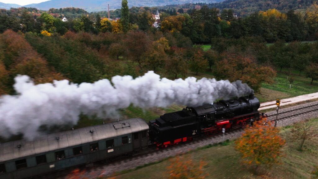 Luftaufnahme eines Dampfzugs mit historischen Personenwagen, der durch herbstliche Obstwiesen in Baden fährt