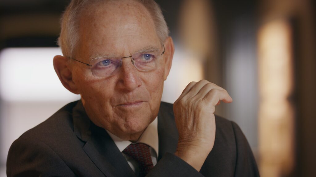 Älterer Interviewpartner mit randloser Brille und Krawatte im Gespräch, Nahaufnahme