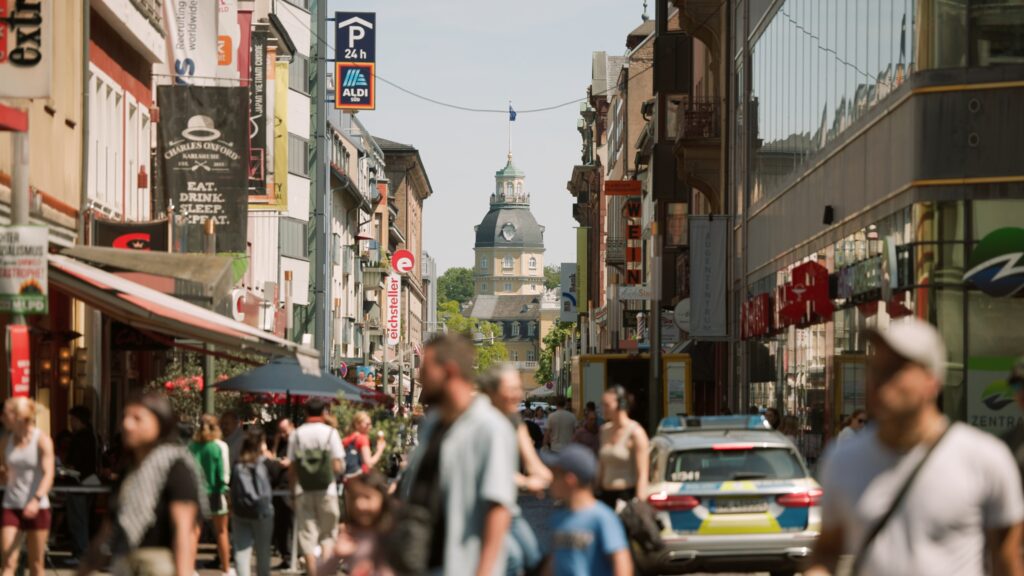 Belebte Fußgängerzone in Karlsruhe mit Blick auf den Turm des Karlsruher Schlosses